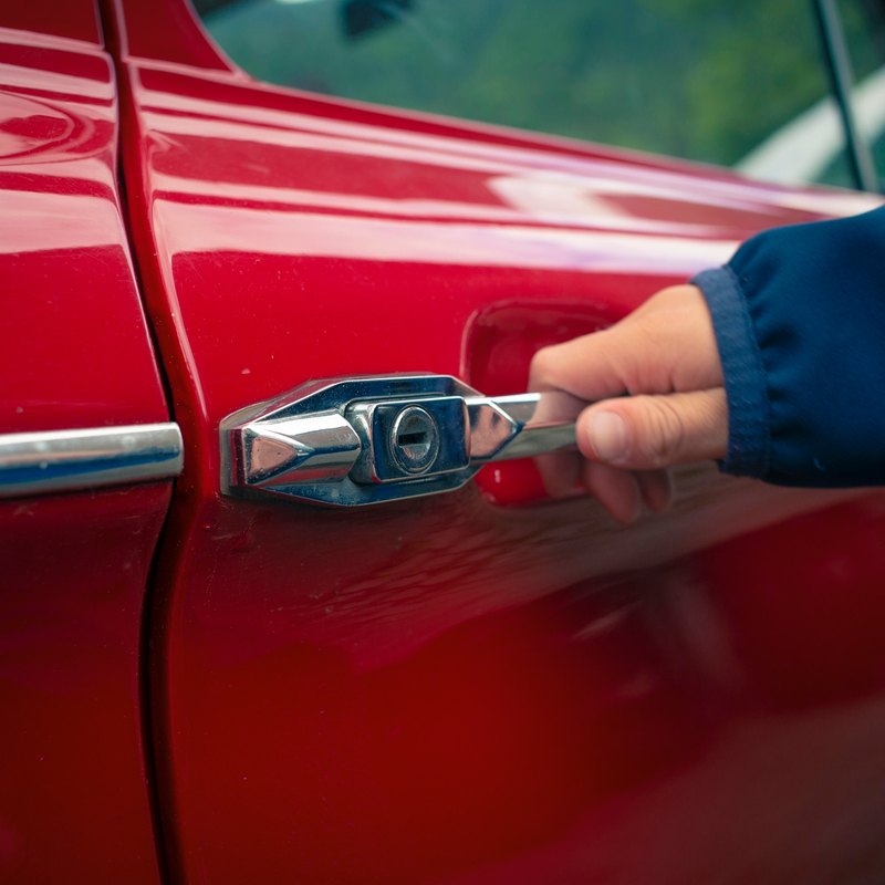 Hand pulling the chrome push-button outside door handle of a red classic car
