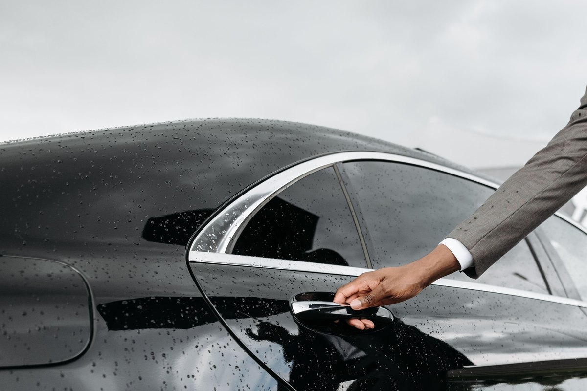 Hand pulling the chrome outside door handle on a black sedan's rear door in the rain