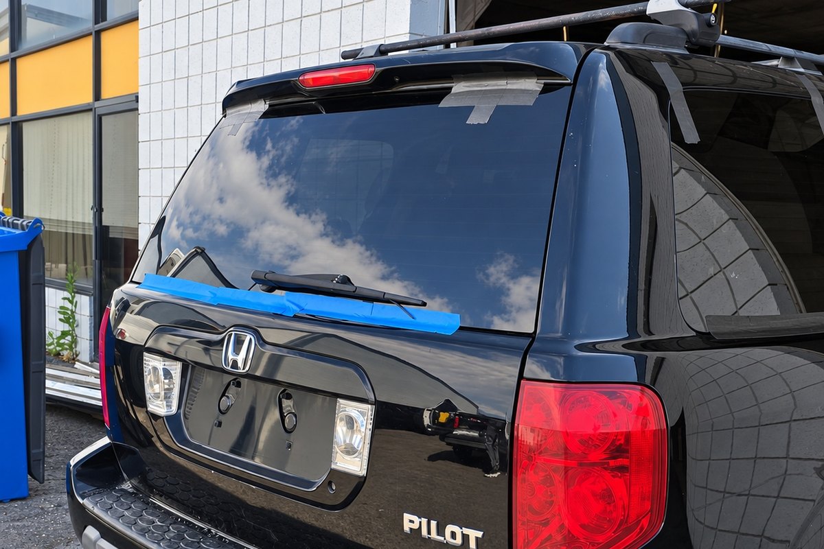 Black Honda Pilot with newly fitted back glass held by blue tape along the bottom