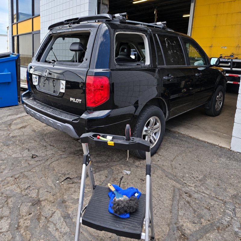 Black Honda Pilot with its back glass and rear side window both missing at a work bay