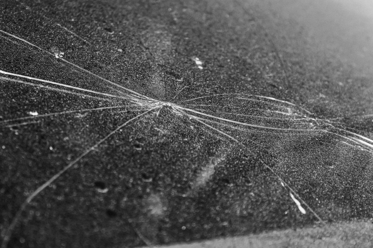 Long cracks spreading across dusty windshield glass from one impact point