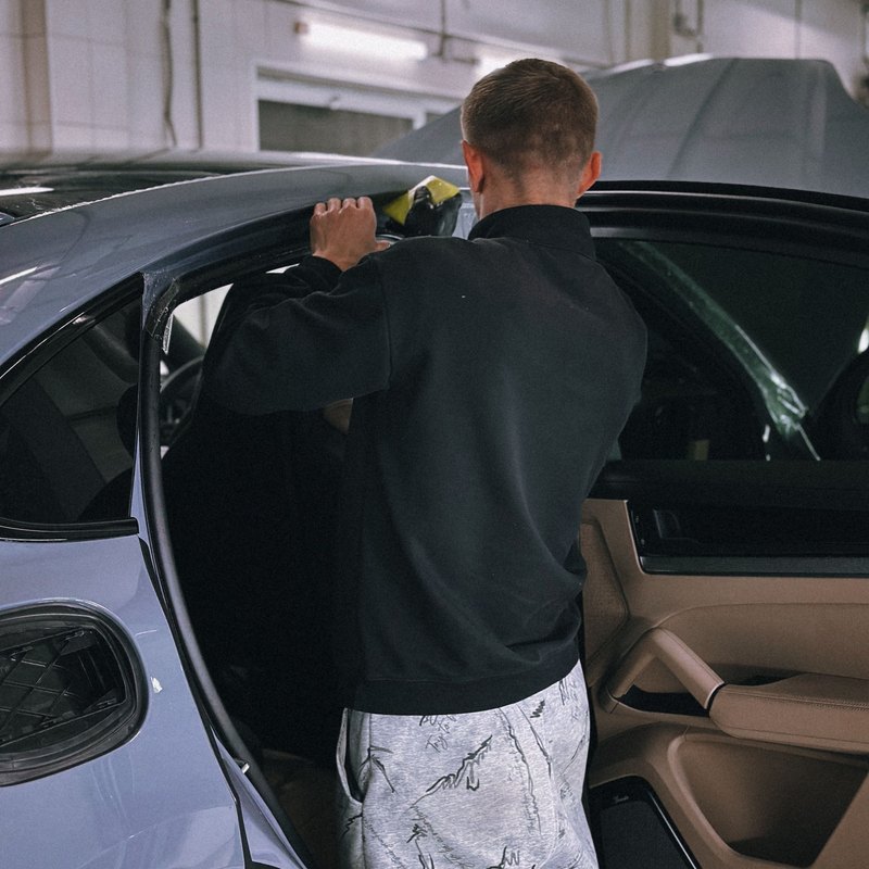 Man reaching to the top of an open rear door's window opening on a pale blue-gray car