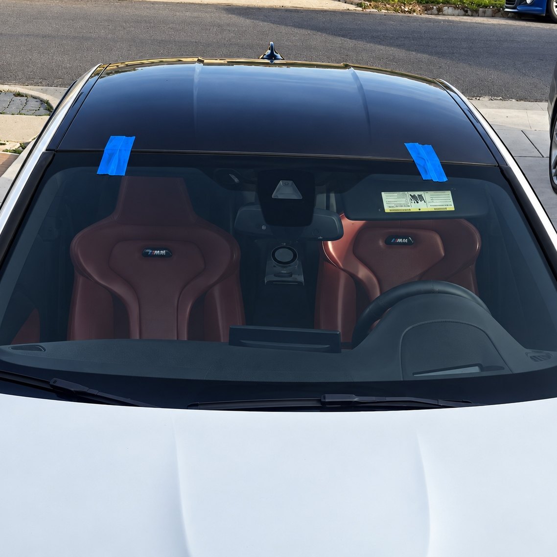 White BMW coupe seen from above with its newly fitted windshield held by blue tape