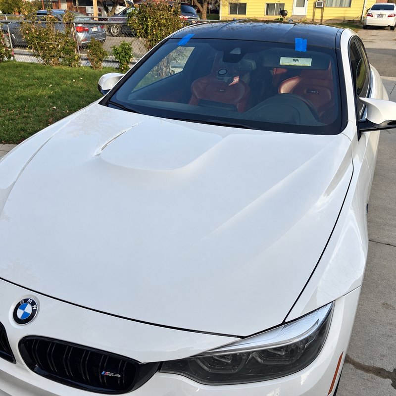 White BMW M4 from above, its newly fitted windshield held by two strips of blue tape