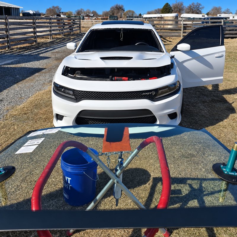 White Dodge Charger with its windshield out and the new glass on a stand at a rural property