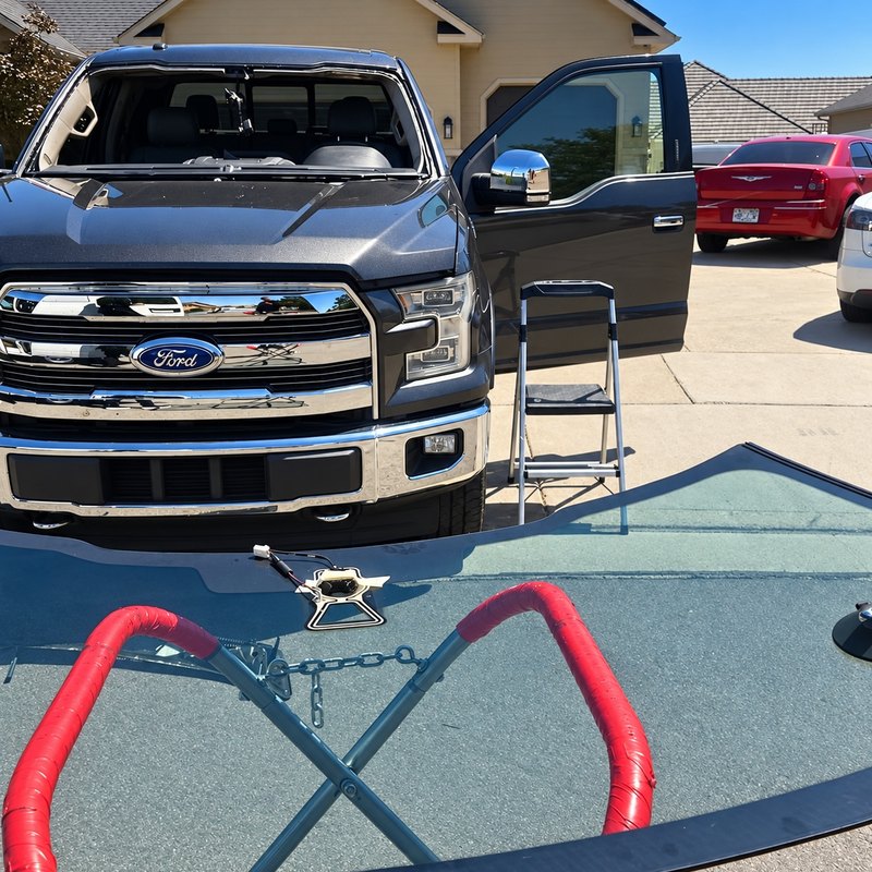 Dark gray Ford F-150 with its windshield removed and the new glass on a stand
