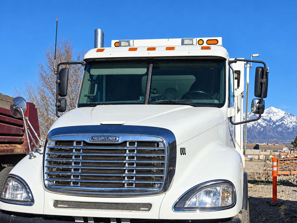White Freightliner work truck with its two-piece windshield in place on a gravel lot