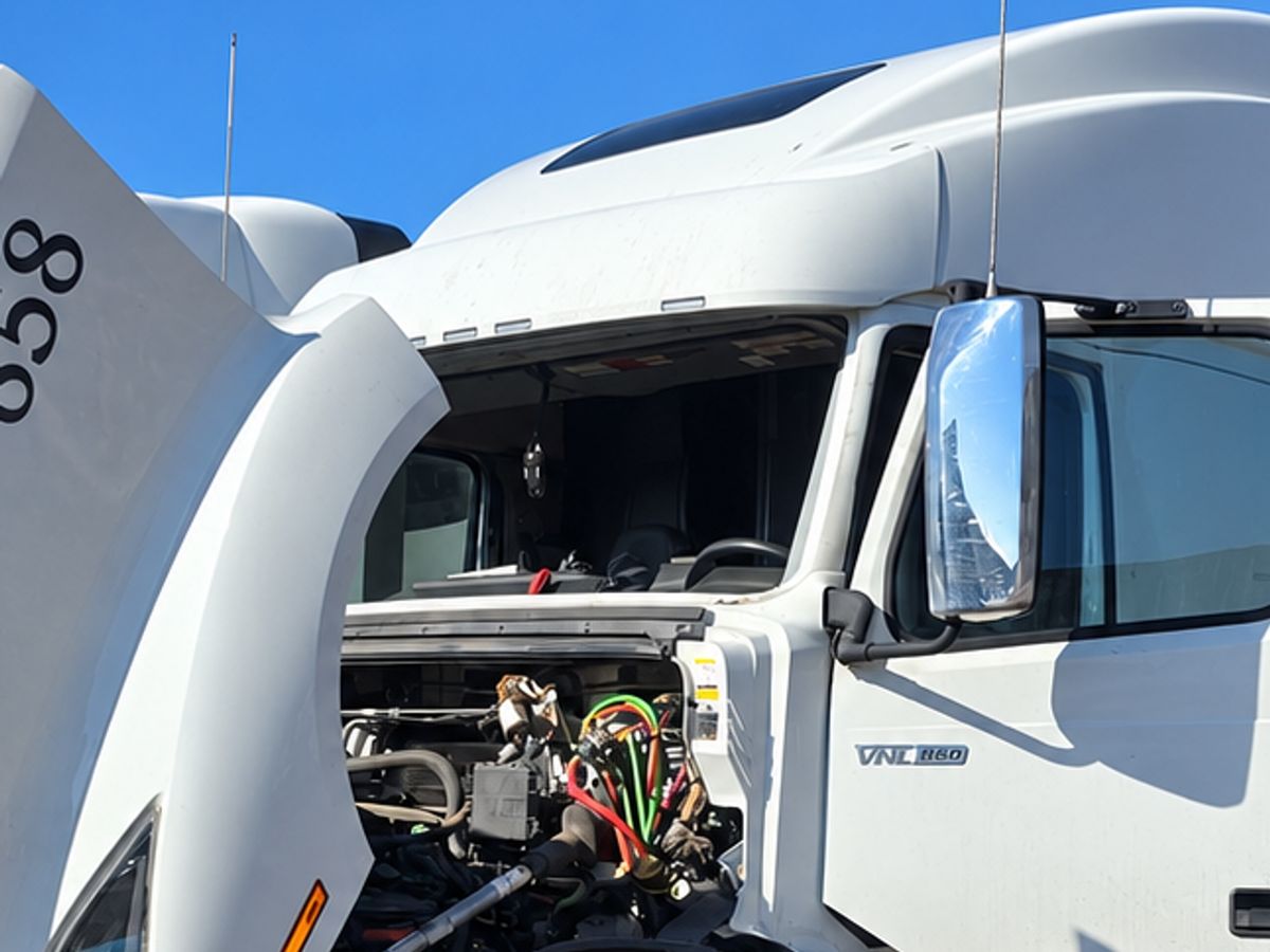 White Volvo sleeper truck on a dirt lot with its hood tilted forward and its windshield out