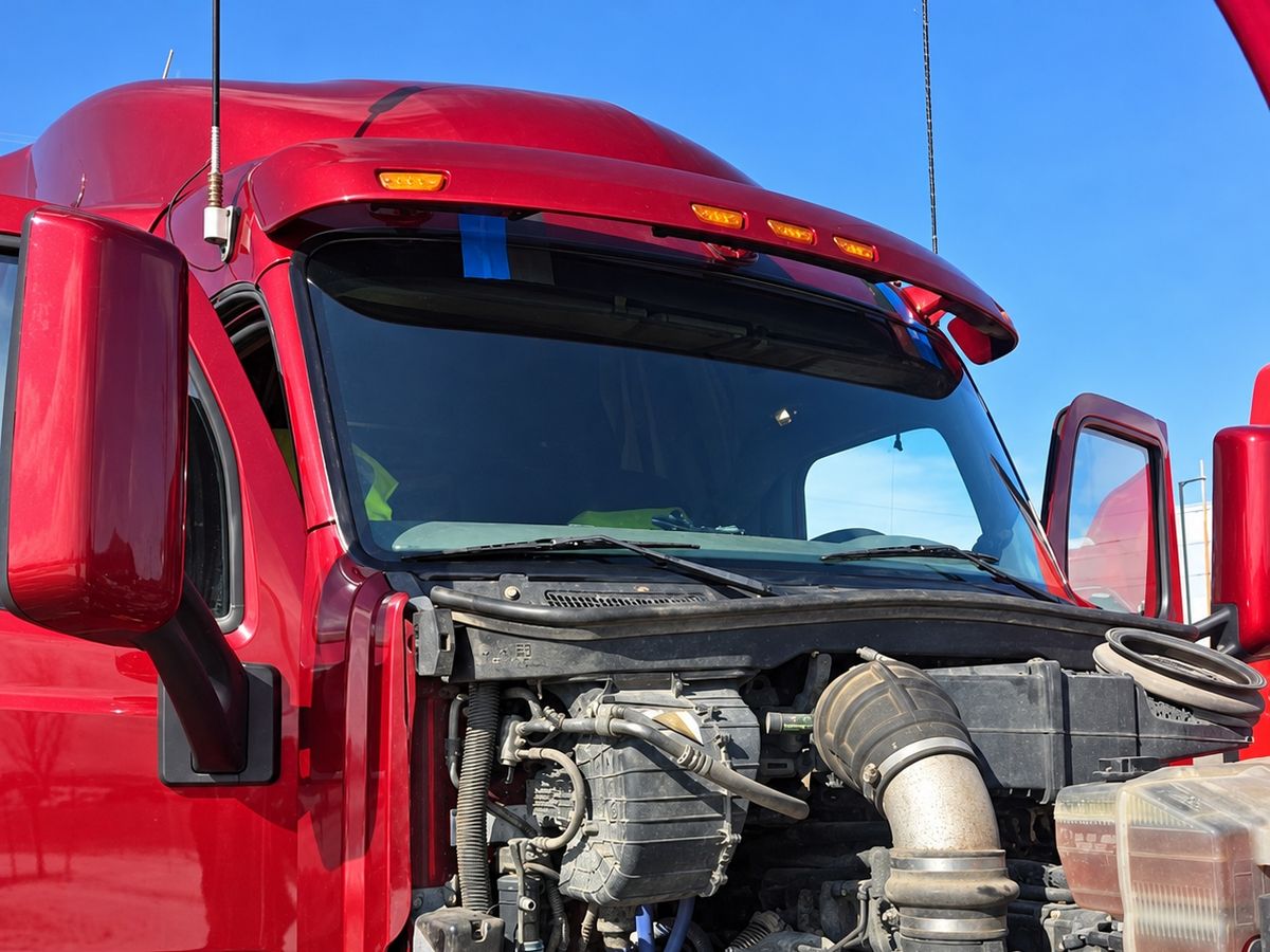 Red semi truck with its hood tilted forward under a newly fitted one-piece windshield