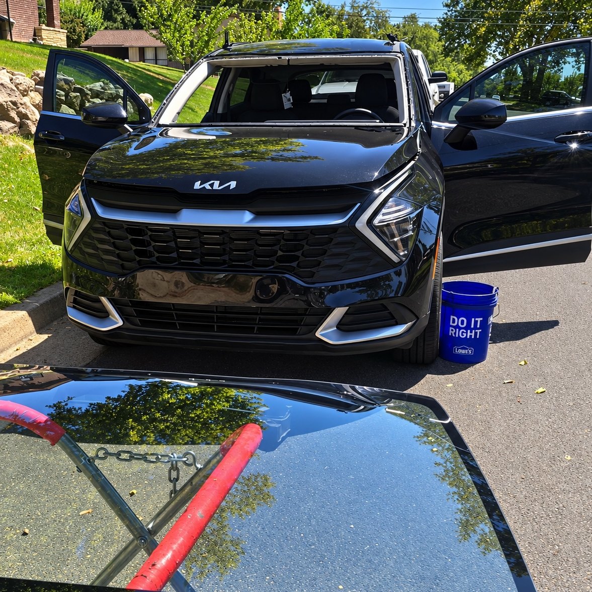 Black Kia SUV at a curb with its windshield removed and the new glass on a stand
