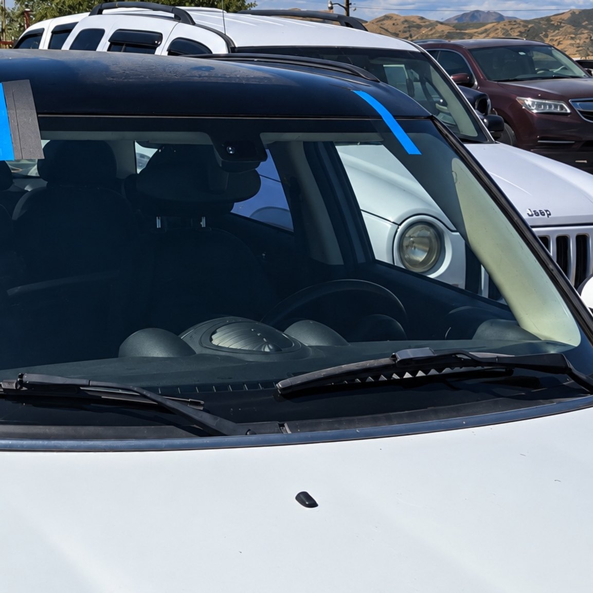 White Mini Countryman with a black roof and a newly fitted windshield held by blue tape, parked beside other cars