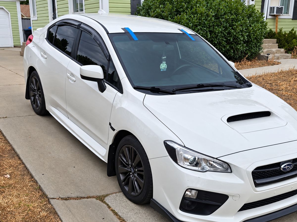 White Subaru WRX in a home driveway with its newly fitted windshield taped at the top