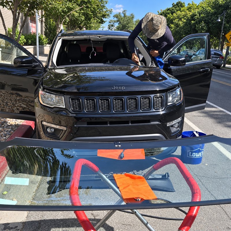 Technician wiping the empty windshield frame of a black Jeep Compass at a city curb