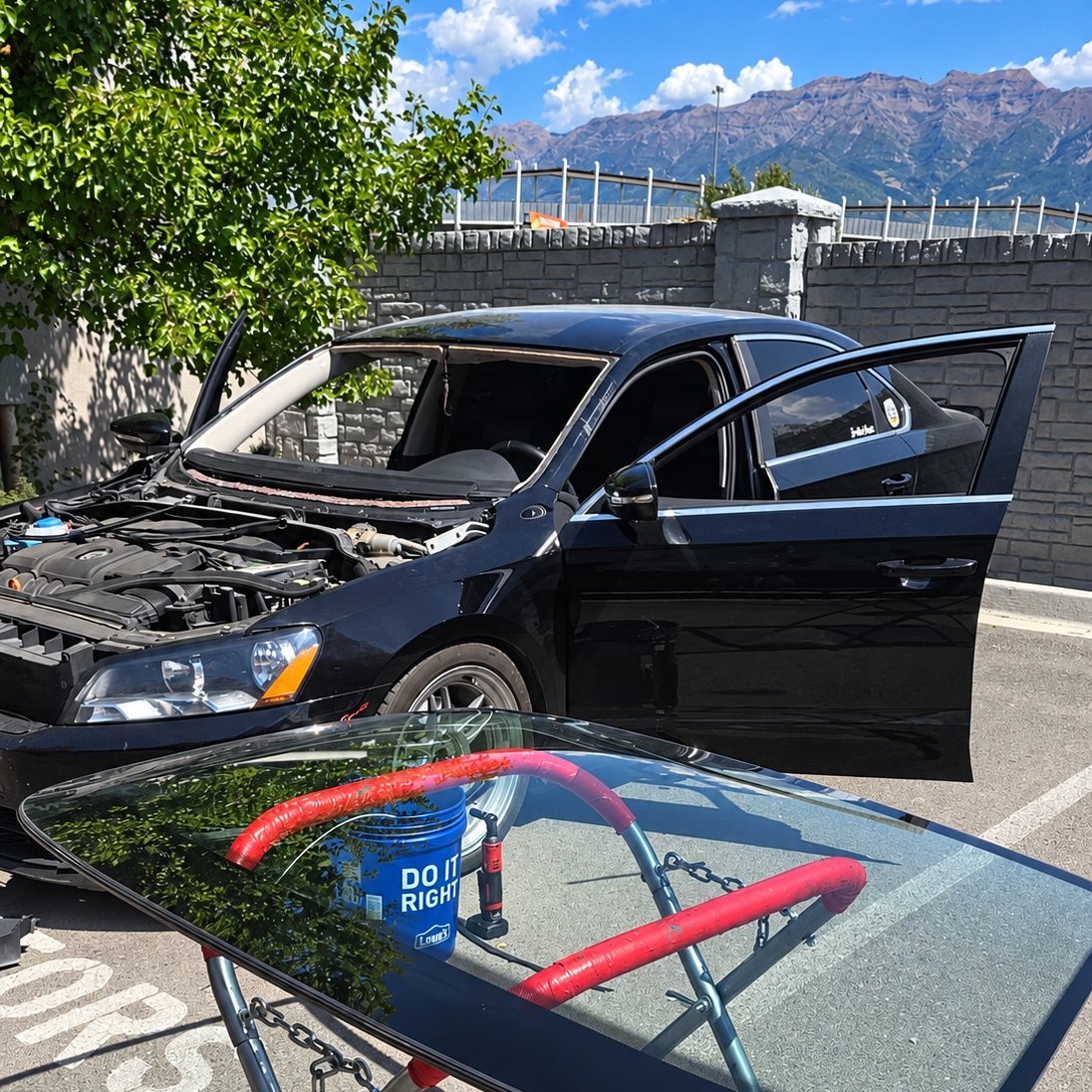 Black Volkswagen sedan with its windshield out and the new glass on a stand below mountains